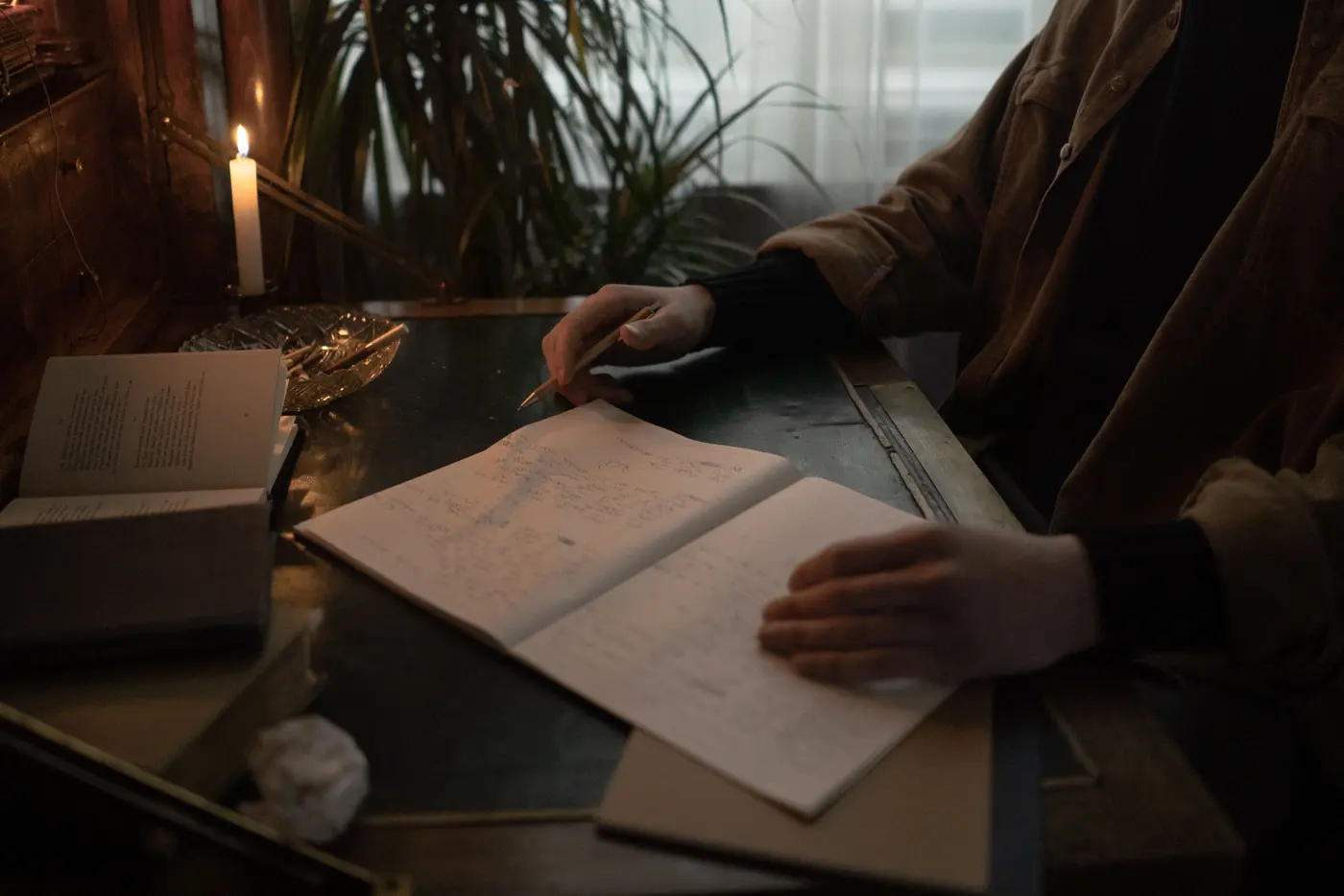 A writer drafting by hand at a candlelit desk