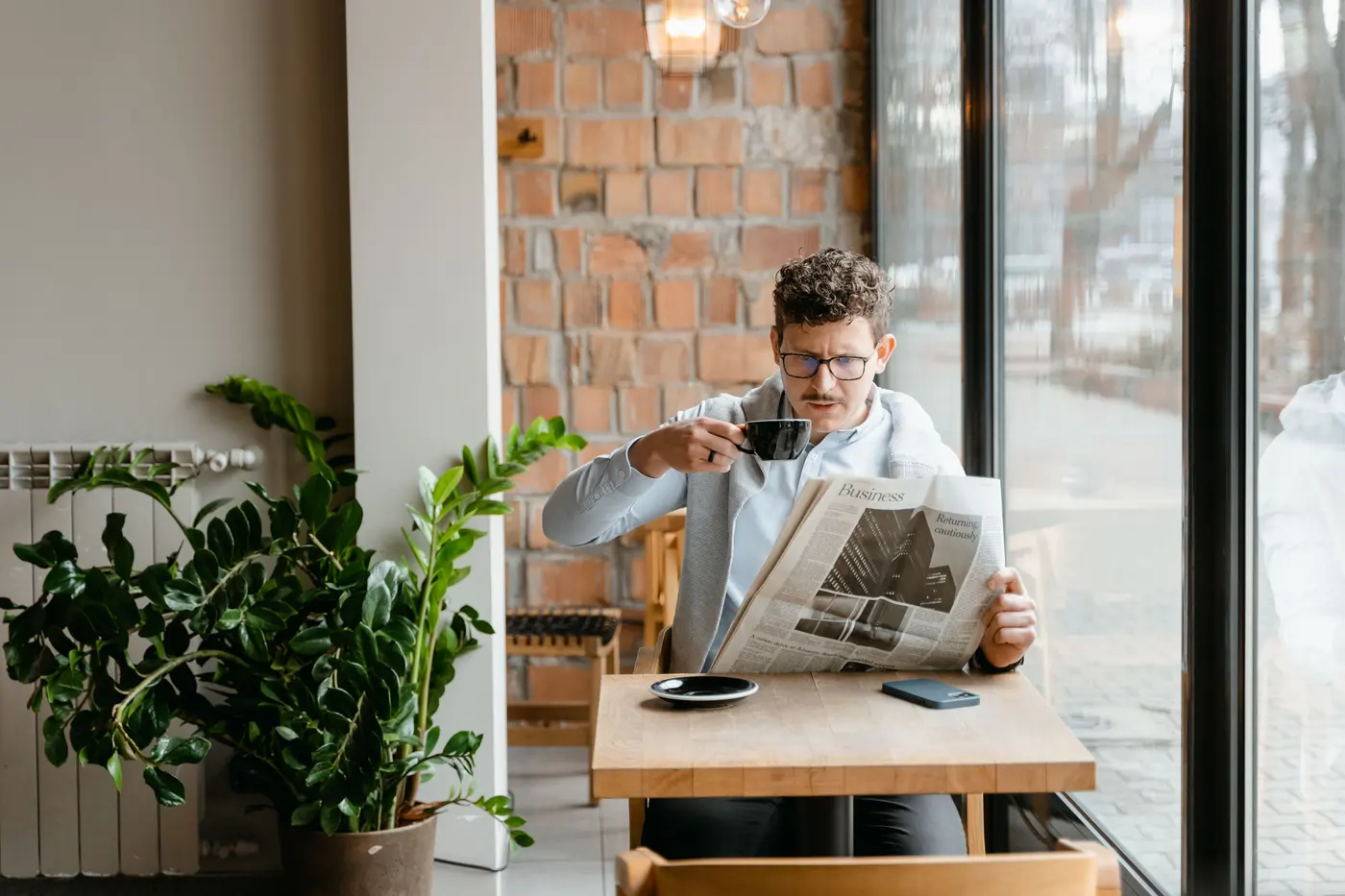 A reader with a newspaper and coffee by a cafe window